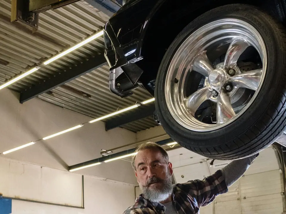 Un meccanico al lavoro sotto la ruota di un’auto sollevata sul ponte