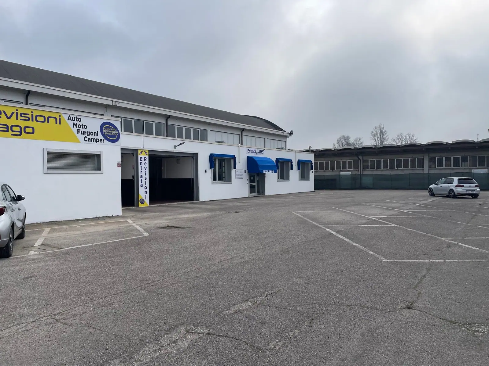 L’esterno del Centro Revisioni Legnago: l’insegna gialla e bianca con la scritta Revisioni Legnago, «Auto Moto Furgoni Camper» e il logo, l’entrata revisioni e l’ingresso uffici sul piazzale con le strisce dei posti auto